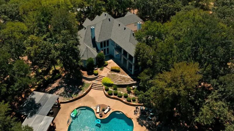 Aerial view of a large brick home with a newly completed grey architectural shingle roof, surrounded by mature oak trees