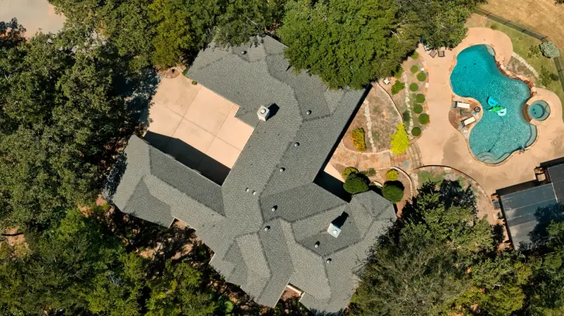 Overhead view of a finished grey shingle roof on a large home with a pool and landscaped patio alongside