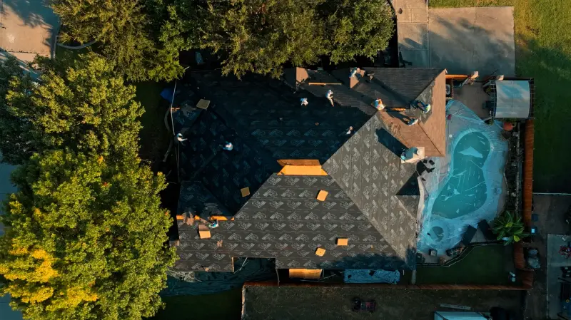 Overhead view of a TDC crew mid-replacement, old shingles stripped and synthetic underlayment rolled across most of the roof deck