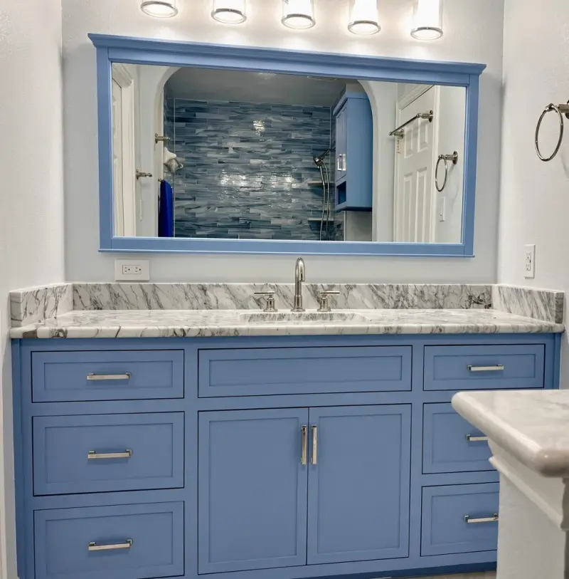 Remodeled bathroom with a blue shaker vanity, a gray marble-look counter, blue glass tile and a framed mirror