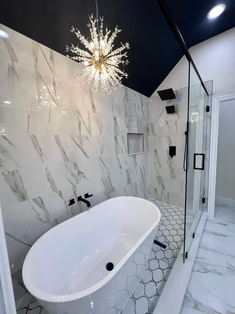 Remodeled bathroom with white marble-look wall tile, a freestanding white tub with a black wall-mounted filler, and a glass shower with black fixtures and a niche