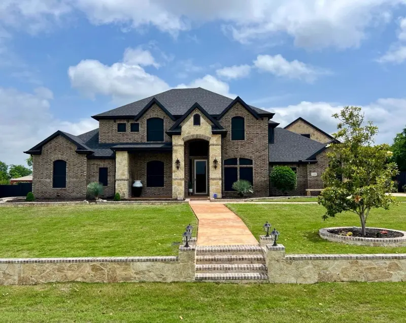 Front view of a large two-story brick and stone home with a new dark shingle roof and a stone walkway up to the entry