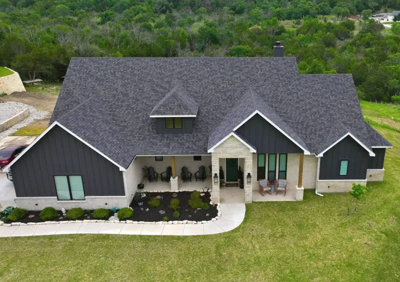 Drone view of a finished gray shingle roof on a modern farmhouse with black board and batten siding and a covered front porch