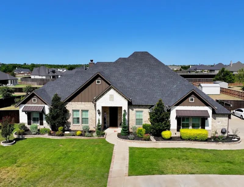 Front view of a single-story stone home with a new dark shingle roof, a covered entry and fresh landscaping