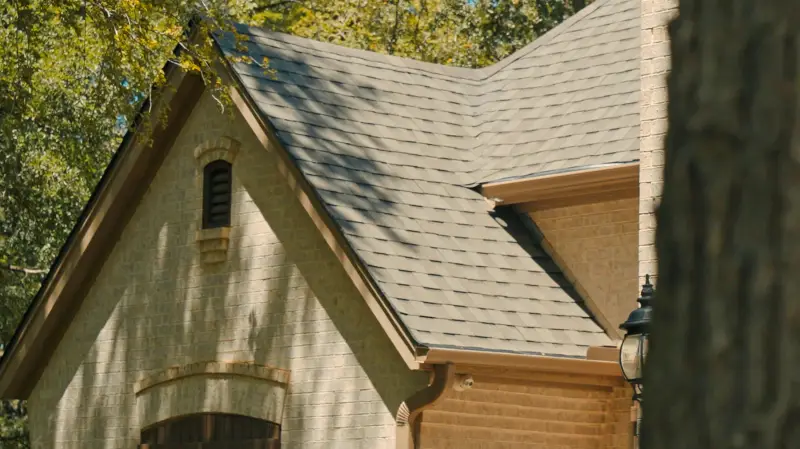 Close view of a completed architectural shingle roof on a cream brick home, with clean gutter lines and a gable vent