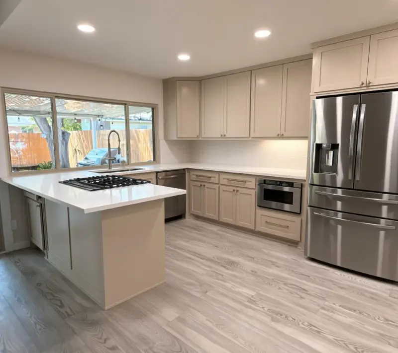 Remodeled kitchen with light gray shaker cabinets, white counters, a gas cooktop on the peninsula, white subway tile backsplash, a stainless refrigerator and light wood-look floors