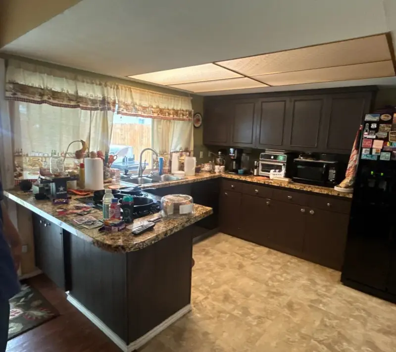 The same kitchen before the remodel, with dark cabinets, granite counters, a drop ceiling with fluorescent panels and beige vinyl floors